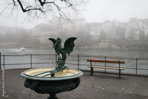 city fountain basel switzerland, foggy day with rhine river and old town in background