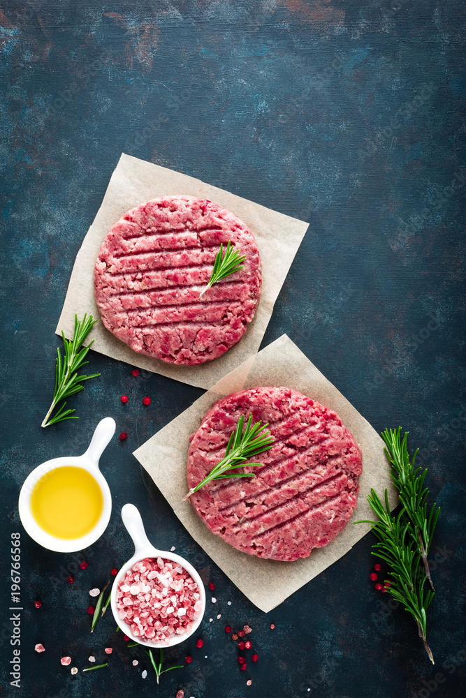 Fresh minced beef meat burgers with spices on dark background. Raw ground beef meat. Flat lay. Top view