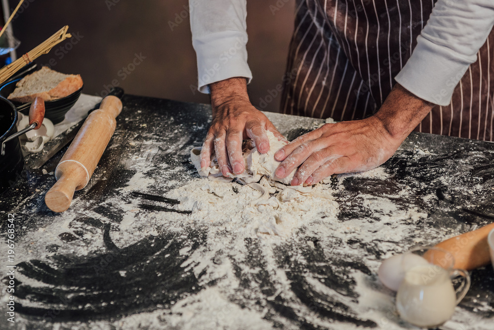 Man preparing buns at table in bakery, Man sprinkling flour over fresh dough on kitchen table Man preparing buns at table in bakery, Man sprinkling flour over fresh dough on kitchen table