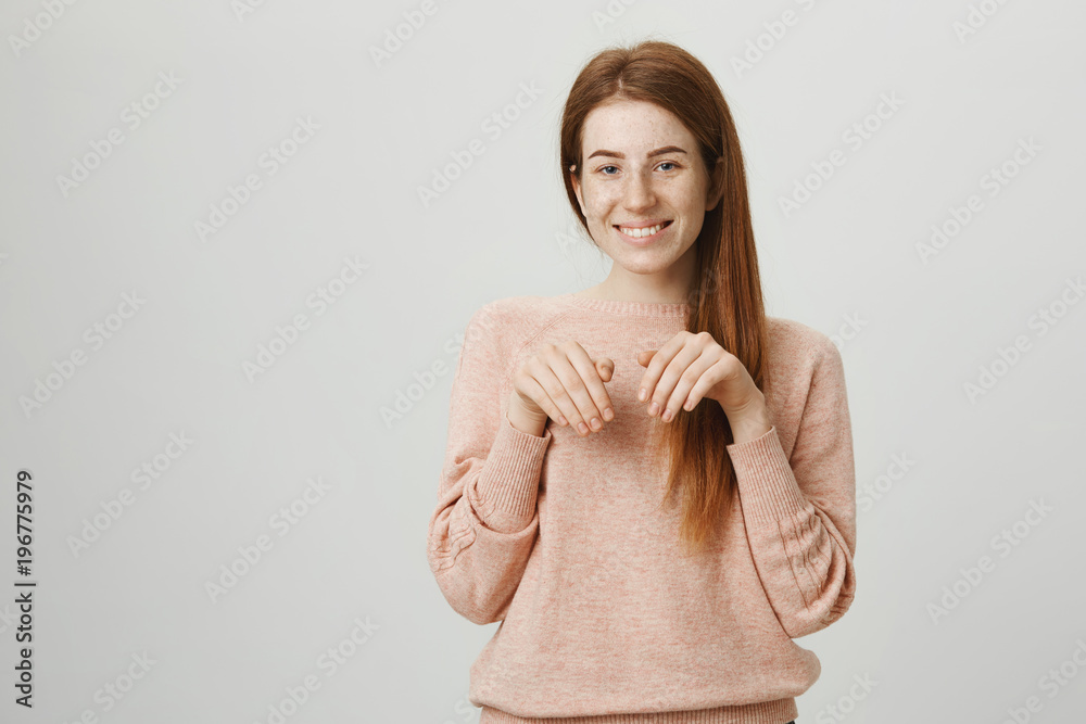 Cute attractive european ginger girl with adorable expression, holding hands near chest as if it is paws, imitating rabbit or puppy, smiling broadly and standing over gray background. Cute attractive european ginger girl with adorable expression, holding hands near chest as if it is paws, imitating rabbit or puppy, smiling broadly and standing over gray background.