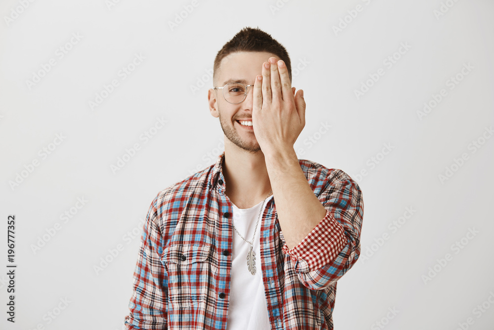 People emotions concept. Portrait of attractive man in glasses hiding half of face with palm while smiling and expressing friendliness. Guy is showing only positive side of his temper People emotions concept. Portrait of attractive man in glasses hiding half of face with palm while smiling and expressing friendliness. Guy is showing only positive side of his temper