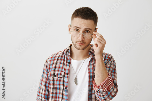 You really mean what you said. Surprised or questioned attractive student taking off trendy glasses and looking at camera as if being stunned with sudden question or revelation over gray wall