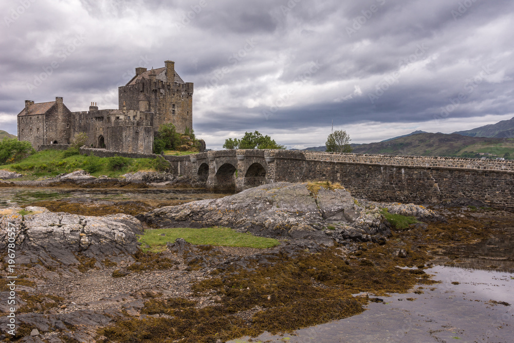 Dornie, Scotland - June 10, 2012: Entire Eilean Donan Castle with footbridge linking green island to mainland. Under rain-heavy dark cloudscape. Dornie, Scotland - June 10, 2012: Entire Eilean Donan Castle with footbridge linking green island to mainland. Under rain-heavy dark cloudscape.
