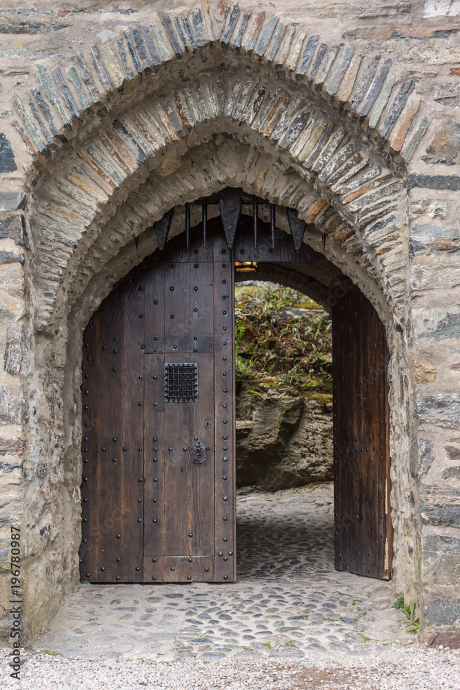 Dornie, Scotland - June 10, 2012: Closeup of gray-stone bowed entrance to Eilean Donan Castle. Brown door open showing some green vegetation.