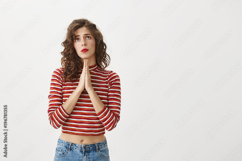 Prayer can make miracles. Studio shot of good-looking european model holding hands in pray and looking up with upset and gloomy expression, being worried and sad while wishing and hoping for better Prayer can make miracles. Studio shot of good-looking european model holding hands in pray and looking up with upset and gloomy expression, being worried and sad while wishing and hoping for better