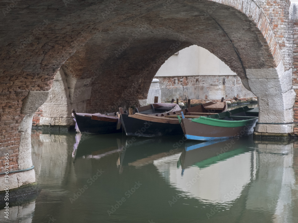 three fishing boats on the canal under an ancient brick arch in Comacchio in Italy