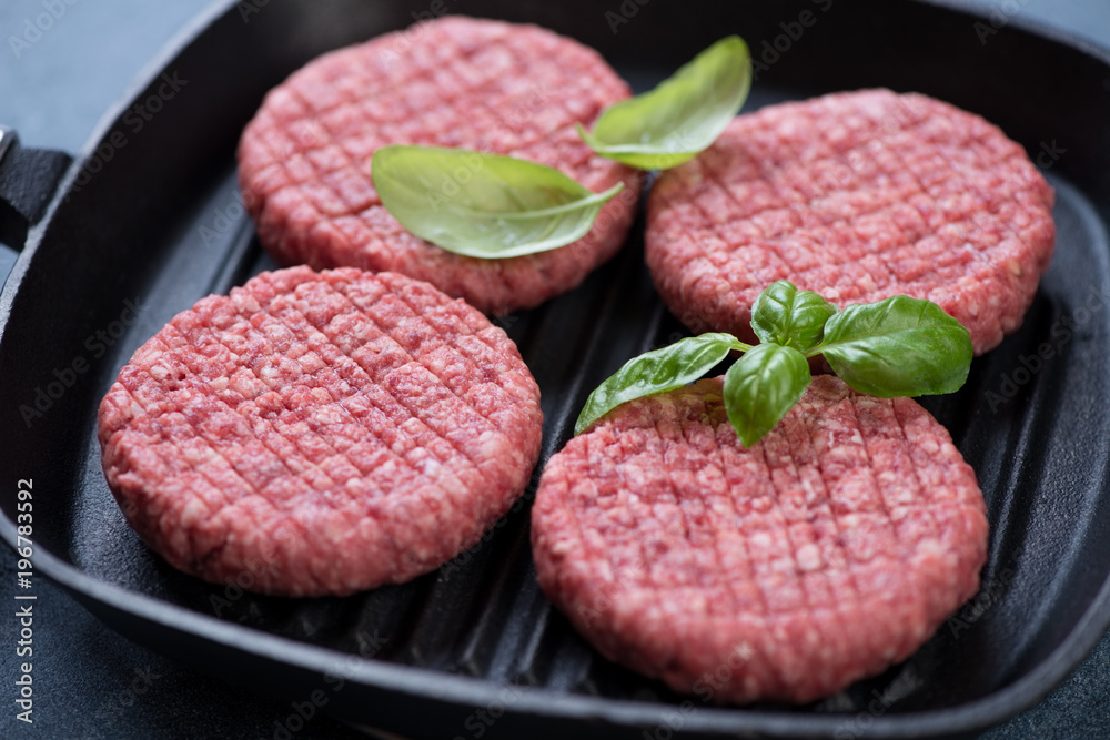 Closeup of raw fresh beef burger cutlets on a cast-iron grill pan ready to be cooked, selective focus Closeup of raw fresh beef burger cutlets on a cast-iron grill pan ready to be cooked, selective focus