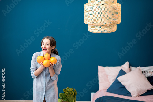 Portrait of a young and happy woman with oranges on the blue wall background at home