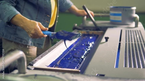 A man is leveling blue paint in a tray of a printing machine photo