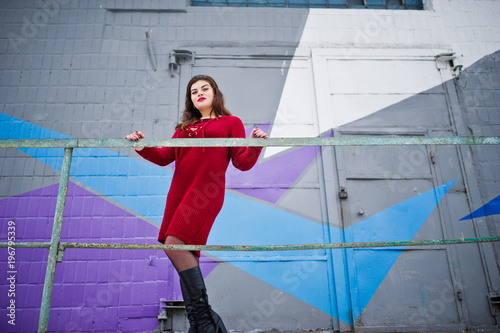 Brunette plus size model at red against colored wall.