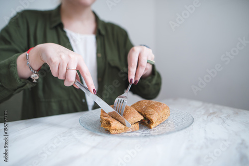 Sewing and knife in the hands of a girl cut a sandwich in a plate. A woman eats a sandwich in a light restaurant. Cutlery in the hands of a close-up. Cut the sandwich with a knife.