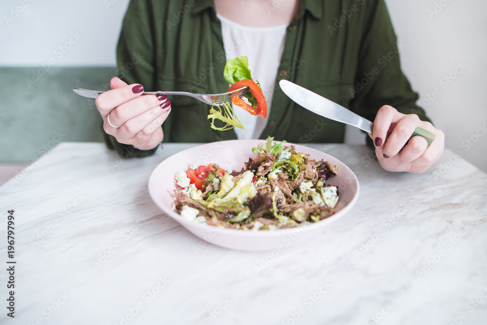 A woman eats a healthy meal for breakfast. Girl and plate of salad on the table. Healthy Eating. A fork with vegetables in a woman's hand close-up