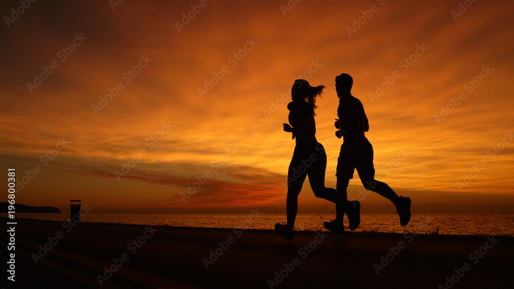 SILHOUETTE: Young man and woman doing their evening workout at gorgeous sunset.