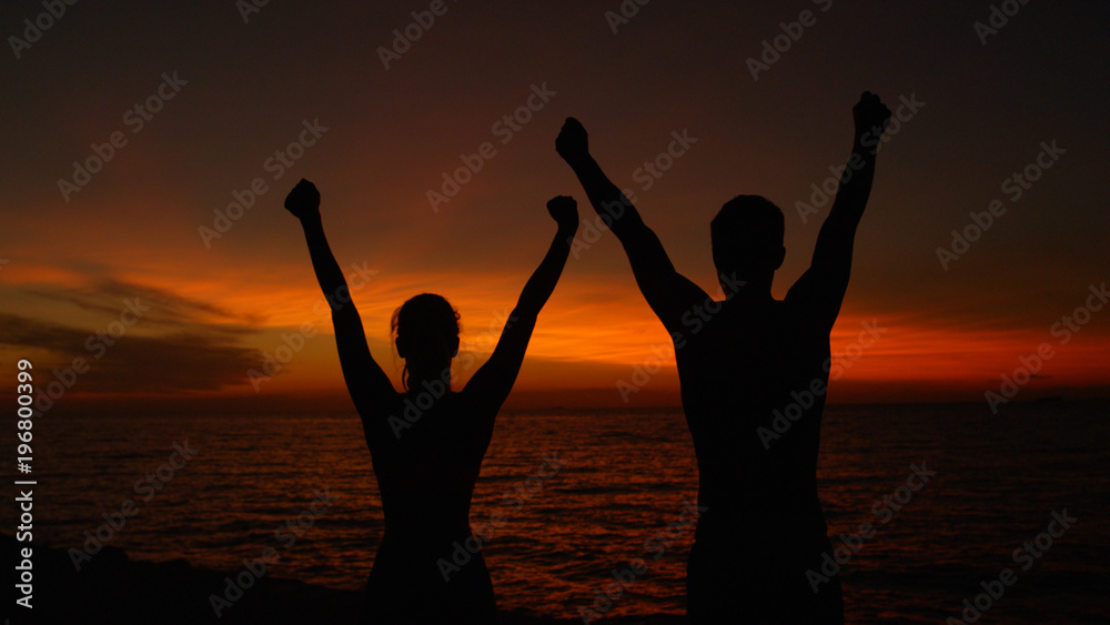 CLOSE UP, SILHOUETTE: Excited couple outstretching arms victoriously at sunset.