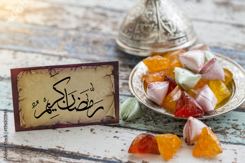 Eid mubarak text in arabic on vintage table with candies on metallic plate photo