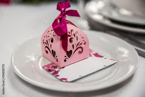 pink bombonniere with a lilac ribbon on a white plate with an invitation card photo