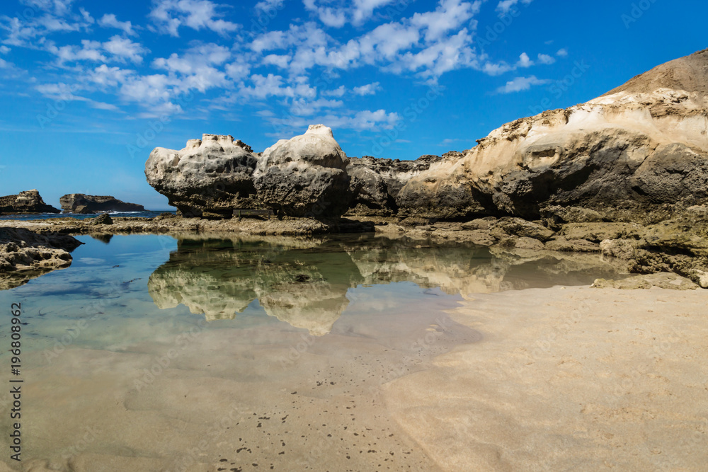 Rock formation with cliff and beach with reflections in the sea at Peterborough beach along the Great Ocean Road, Victoria, Australia Rock formation with cliff and beach with reflections in the sea at Peterborough beach along the Great Ocean Road, Victoria, Australia