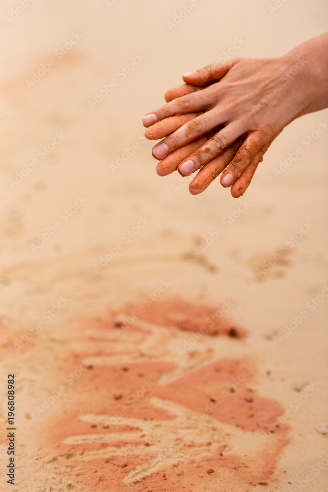 Woman hands creating shapes with red sand on the beach in aboriginal art style
