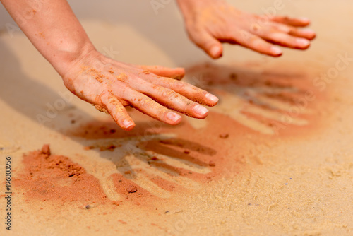 Obraz na płótnie Woman hands creating shapes with red sand on the beach in aboriginal art style w salonie