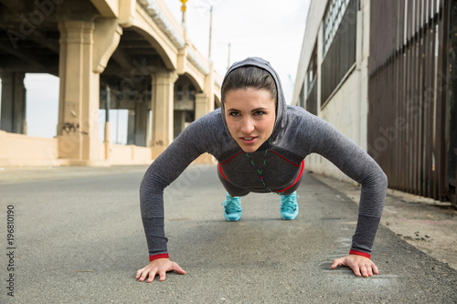 Determined strong female athlete exercising push ups and self training on urban city streets