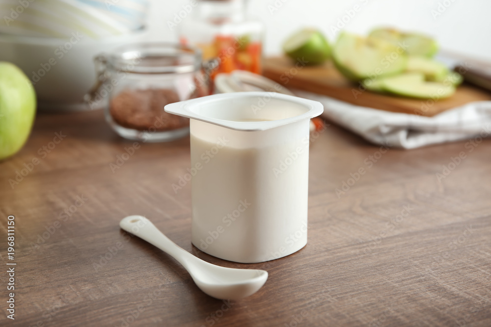 Obraz premium Plastic cup of yummy yogurt on wooden table