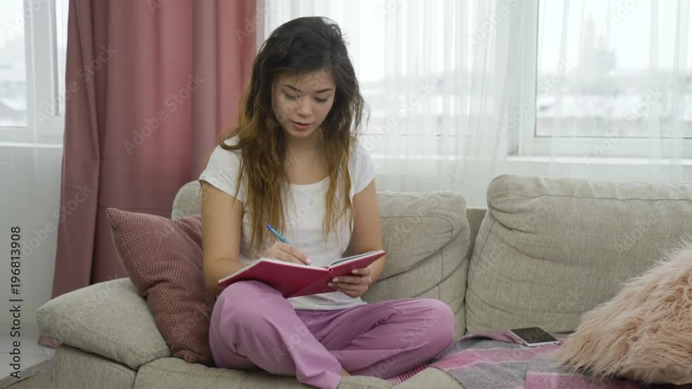 leisure pastime. teenage girl having some me time. relaxed young woman sitting on a couch in comfortable home clothing writing in the notebook leisure pastime. teenage girl having some me time. relaxed young woman sitting on a couch in comfortable home clothing writing in the notebook