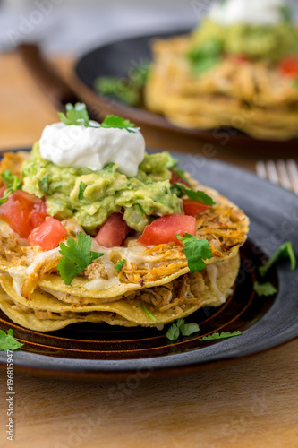 Stacked tostada dish closeup. Tostadas are a type mexican food, made with crispy fried corn tortillas covered with layers of various ingredients such as chicken, guacamole, cheese, sour cream & salsa.