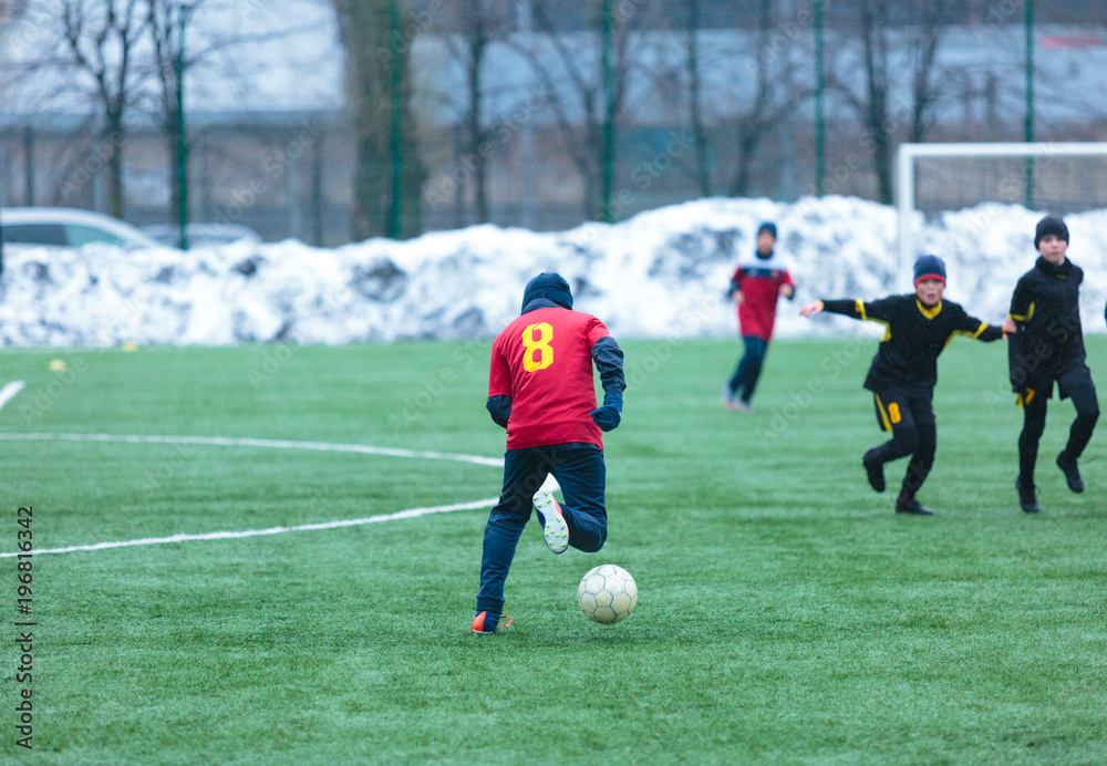  boy in red uniform -football player plays soccer on the green field in the winter