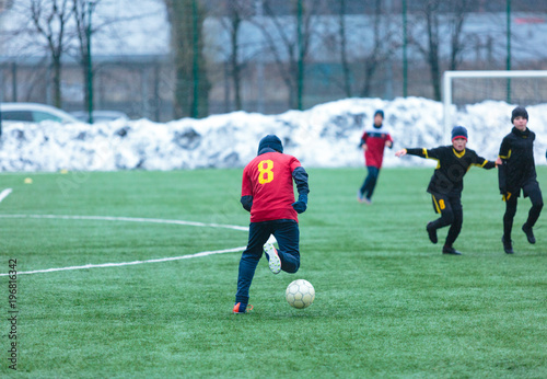  boy in red uniform -football player plays soccer on the green field in the winter © Natali