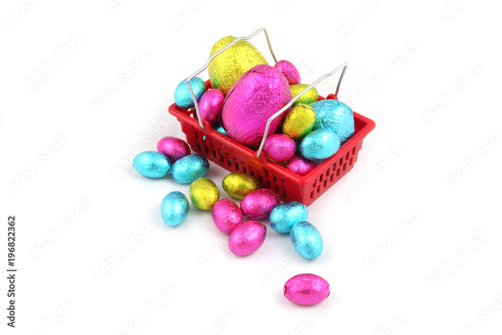 Colourful chocolate easter eggs in foil wrapping, & sitting in a shopping basket from a super market on a white background.