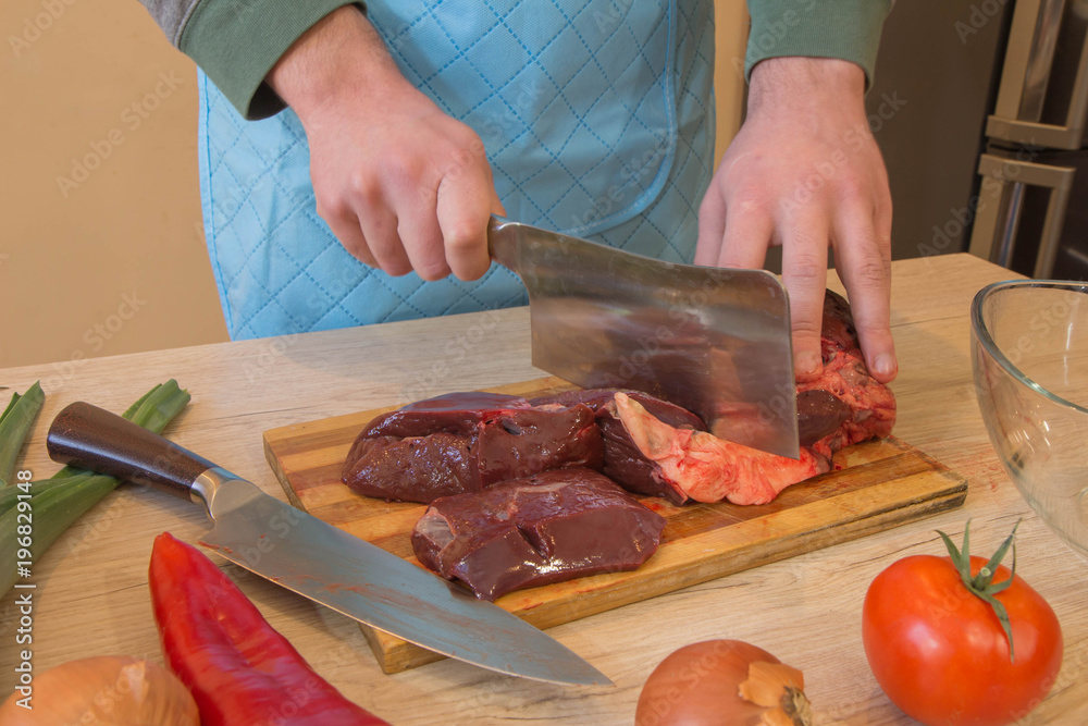Chef's hands with a knife cuts the meat on the wooden board in the kitchen. Cooking at home