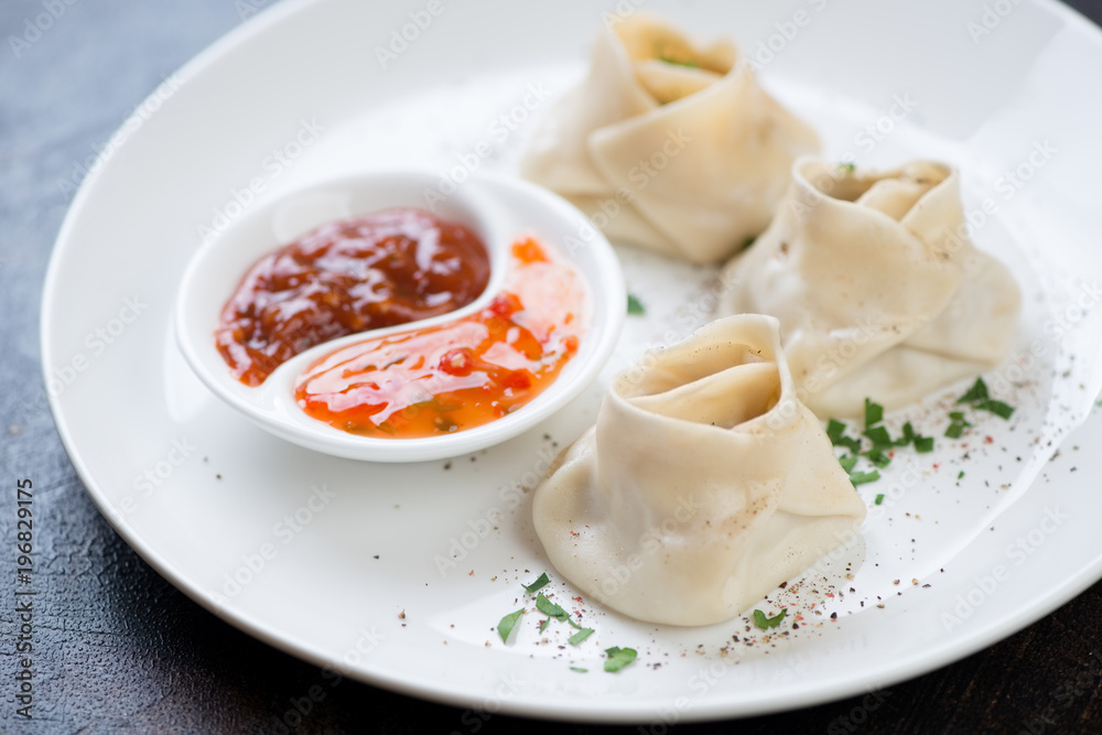 Close-up of manti or steamed meat dumplings with sauce and greens on a white plate, selective focus Close-up of manti or steamed meat dumplings with sauce and greens on a white plate, selective focus
