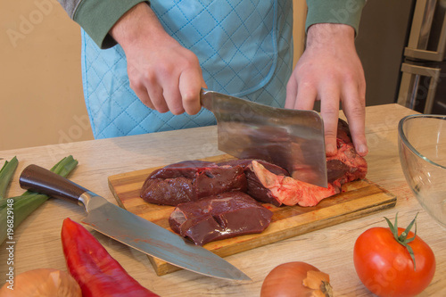 Chef's hands with a knife cuts the meat on the wooden board in the kitchen. Cooking at home