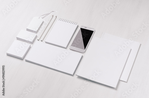 White blank stationery - label  notepad  letterhead  envelop  phone on soft white wooden plank  blank objects for placing your design  inclined. Modern stylish work place.