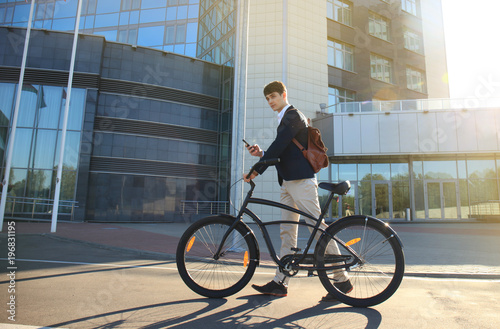 Fototapeta Naklejka Na Ścianę i Meble -  Young businessman with bicycle and smartphone on city street.