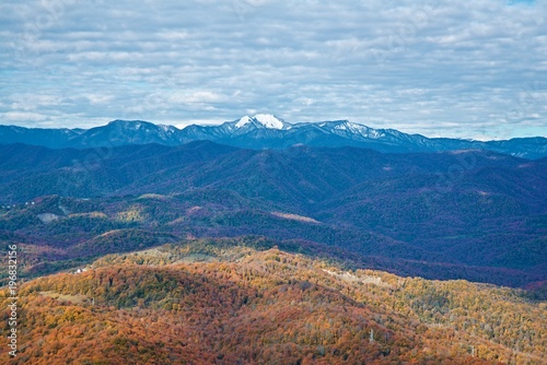 Autumn landscape. Snowy mountains on the horizon and autumn forest near. Blue sky with clouds.