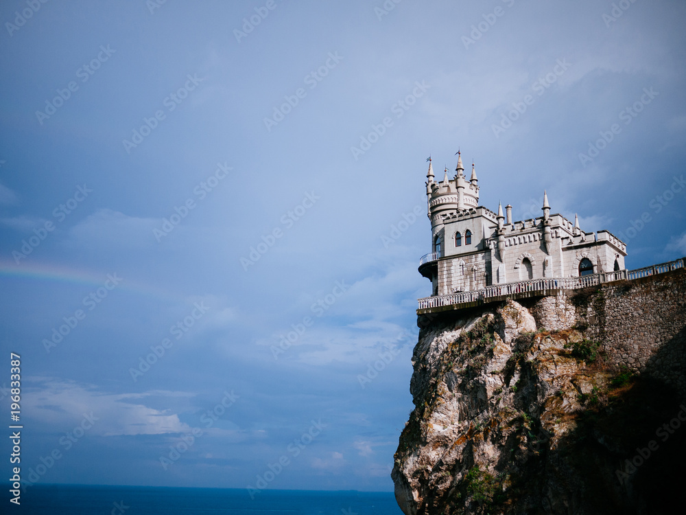 Old castle on the precipice, rainbow. The sky and the sea background
