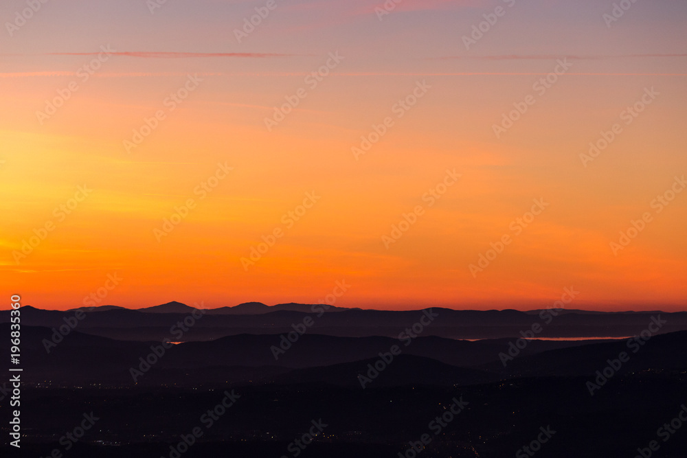 Beautiful aerial view of Umbria (Italy) valley at dusk, with hills, city lights and Trasimeno lake reflecting orange sky light