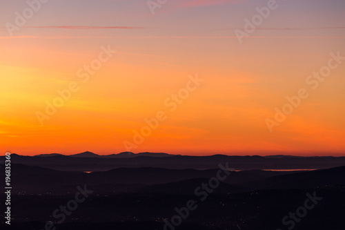 Beautiful aerial view of Umbria (Italy) valley at dusk, with hills, city lights and Trasimeno lake reflecting orange sky light