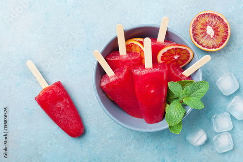 Ice cream or popsicles decorated mint leaves and orange slices on blue table top view. Frozen fruit juice. Summer food.