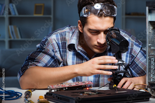 Repairman trying to repair laptop with miscroscope