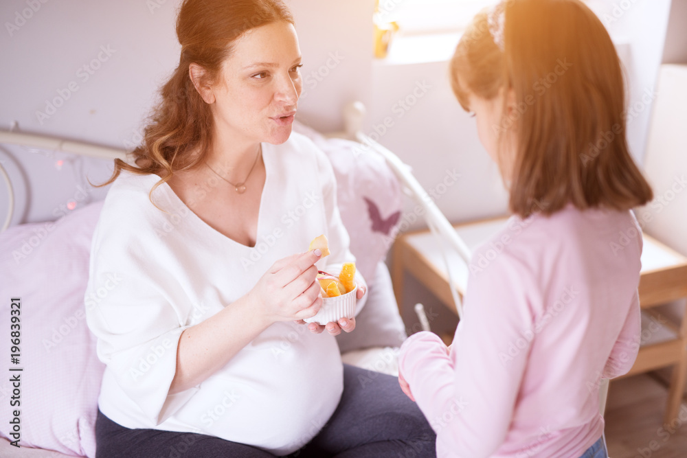 Careful pregnant young woman eating fruit salad with her little toddler daughter. Careful pregnant young woman eating fruit salad with her little toddler daughter.