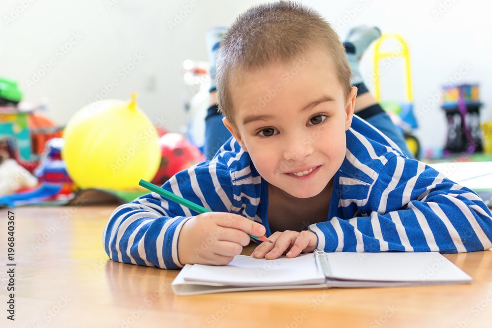 Little boy writing something in notebook on the floor
