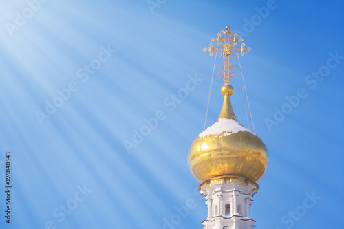 Gilded dome of a Christian temple illuminated by rays of sun against a bright blue sky with copy space