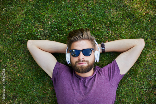 Man and listening to music while lying on the ground outdoors in sunglasses
