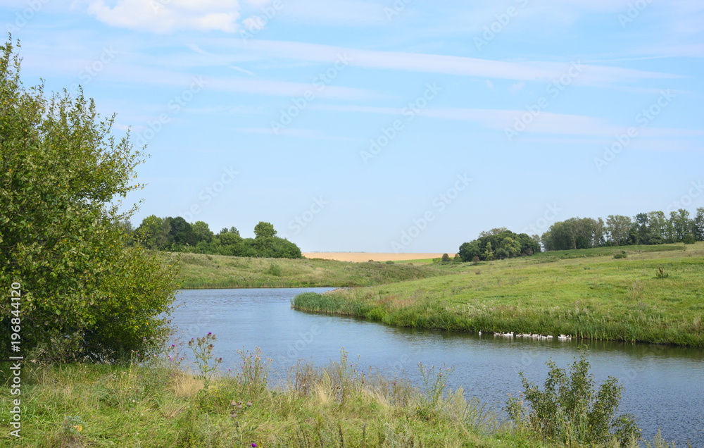 Fototapeta premium Sunny summer landscape.Green hills,fields and meadows.River Krasivaya Mecha in Tula region,Russia.Countryside scene.Bright blue sky with clouds.