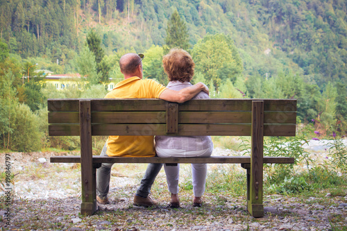 back view of middle aged couple, mature male and woman sitting on a bench outdoor (love concept)
