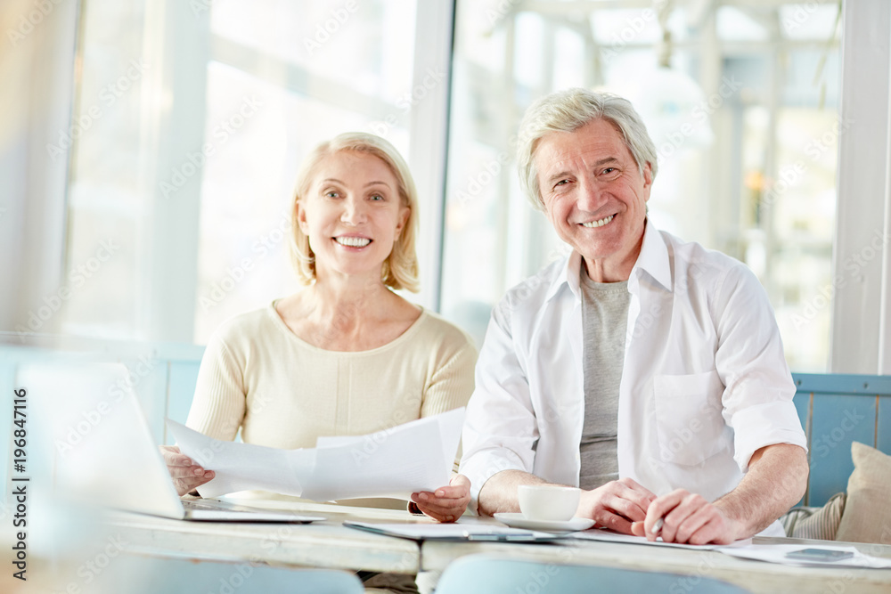 Two aged colleagues looking at camera while working with financial documents at meeting Two aged colleagues looking at camera while working with financial documents at meeting