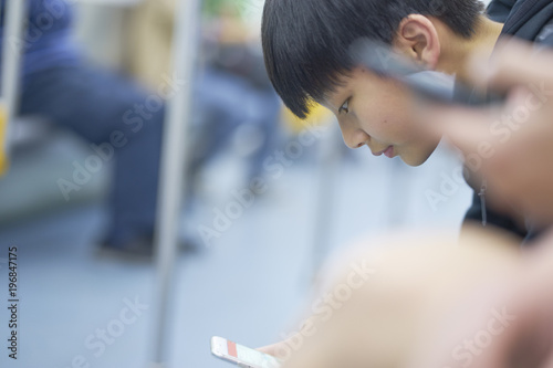 Asian teenage boy using smart phone on the MRT
