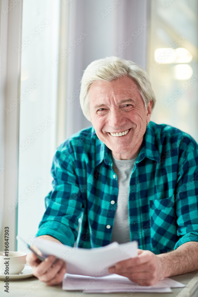 Cheerful aged man with papers looking at camera while spending time in cafe Cheerful aged man with papers looking at camera while spending time in cafe